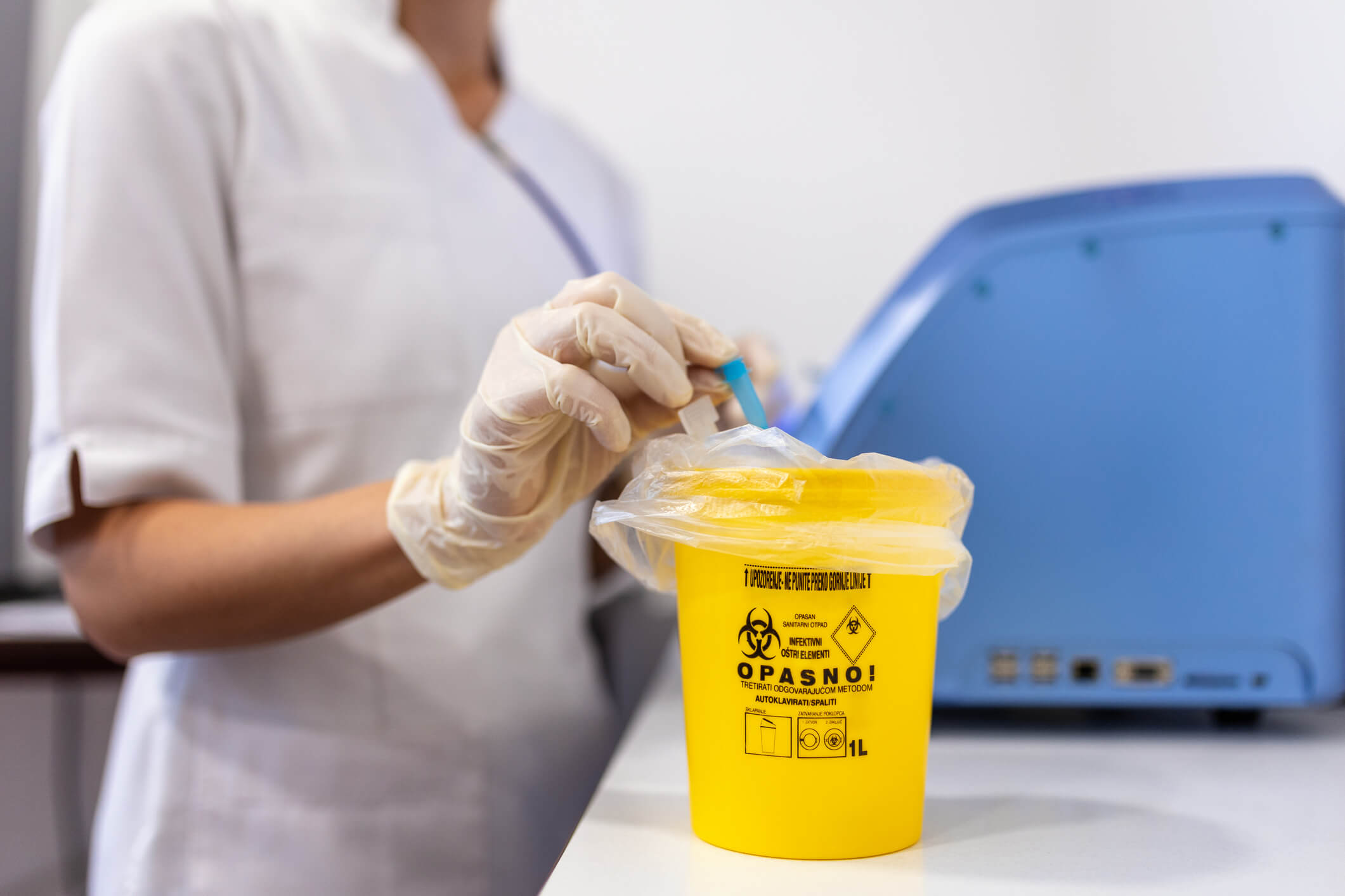 Nurse disposing syringe in yellow medical container.