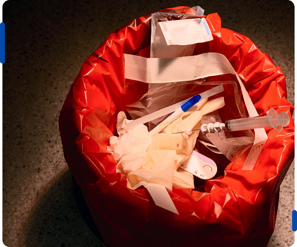 Red biohazard bag filled with medical waste including gloves and syringes.